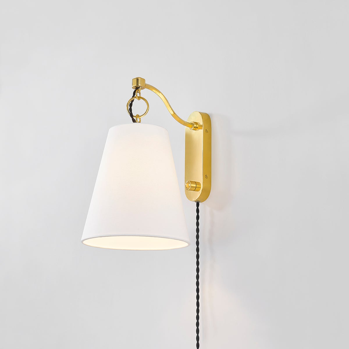 Close-up of the Joan Plug-In Sconce in aged brass showing the arm profile and shade silhouette.