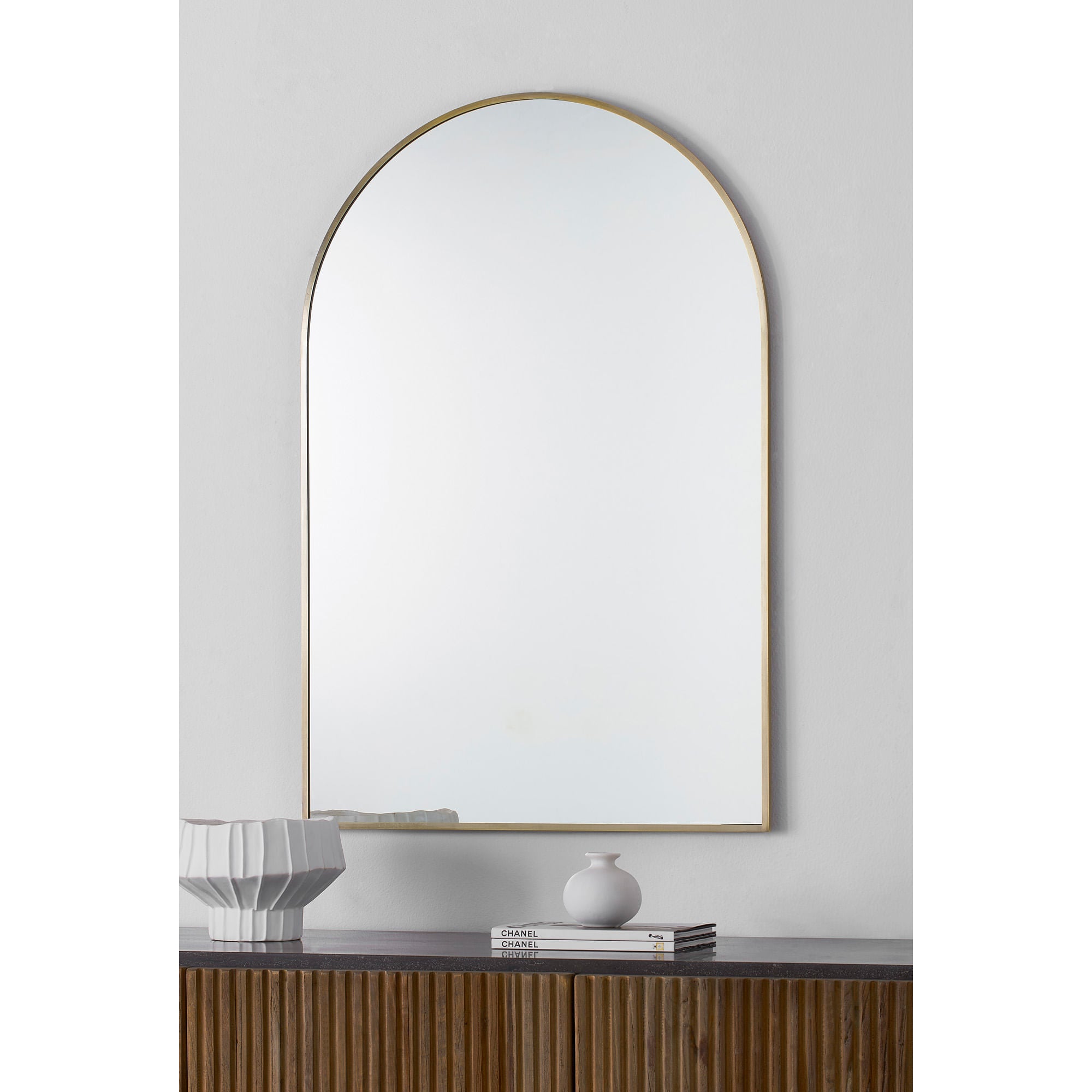 Durness mirror with an arched gold frame, reflecting light against a neutral wall, displayed above a wooden console.