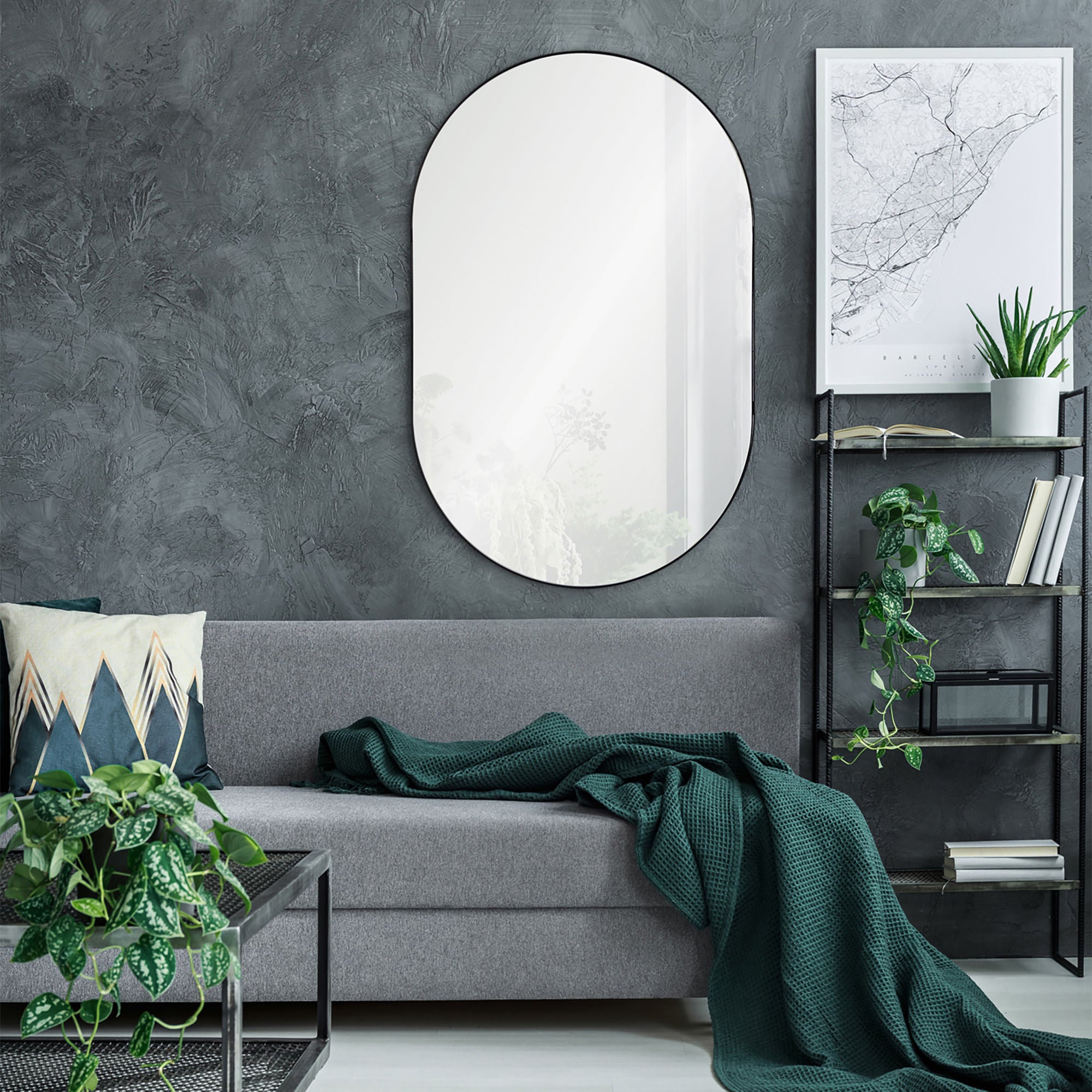 Webster mirror with an oval shape and black frame, mounted on a textured gray wall above a gray sofa with a green blanket.