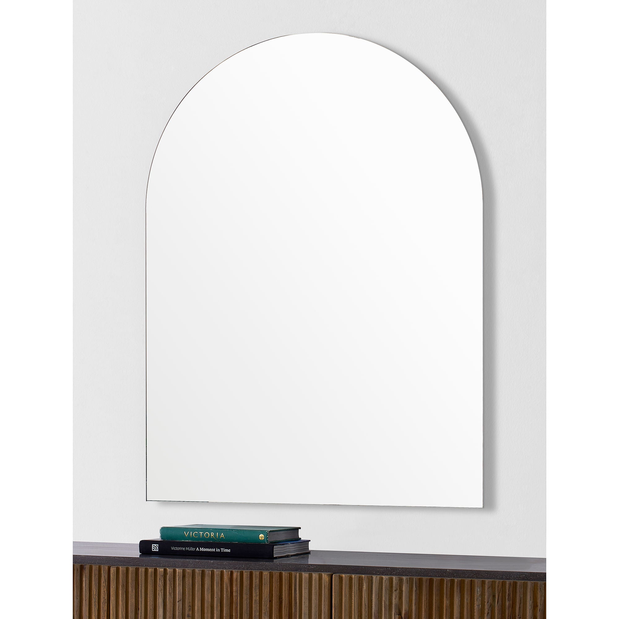 Aldrin mirror mounted on a wall above a wooden shelf with books.