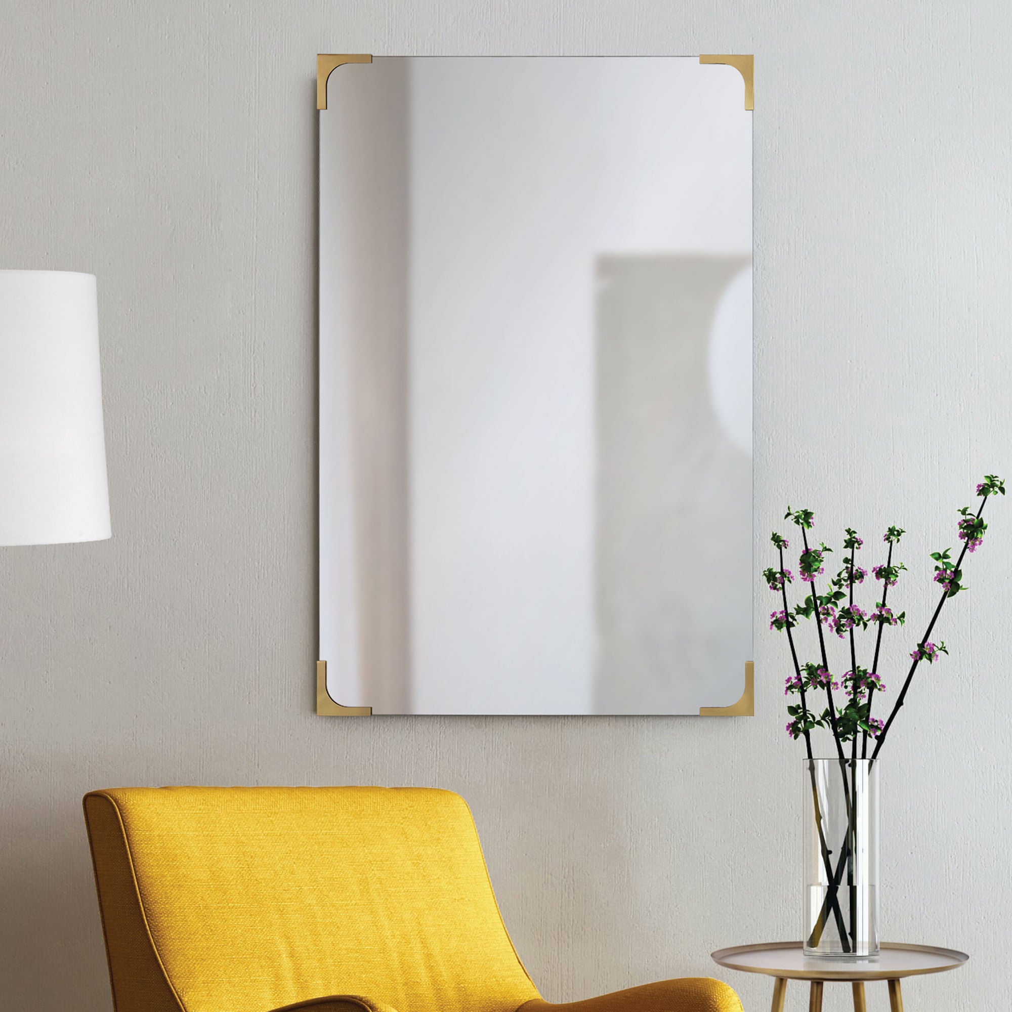Eros mirror mounted on a wall beside a yellow chair and floral decor.