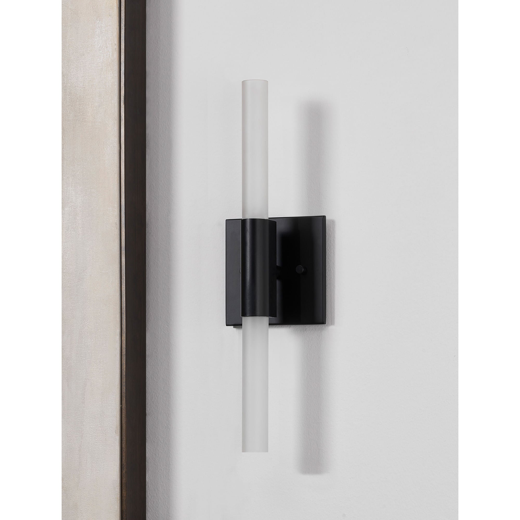 Lina wall sconce by Renwil, mounted on a wall, featuring matte black base and frosted glass tube.