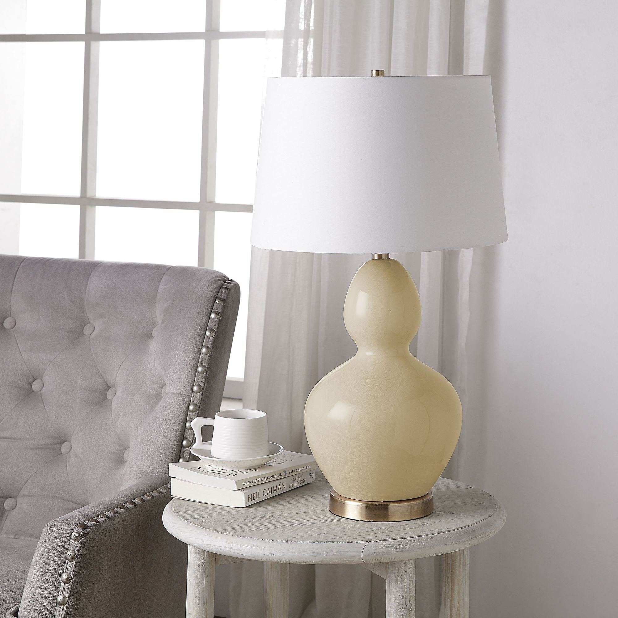 Jesula Table Lamp Set - cream ceramic base with white shade, placed on a side table next to a gray chair