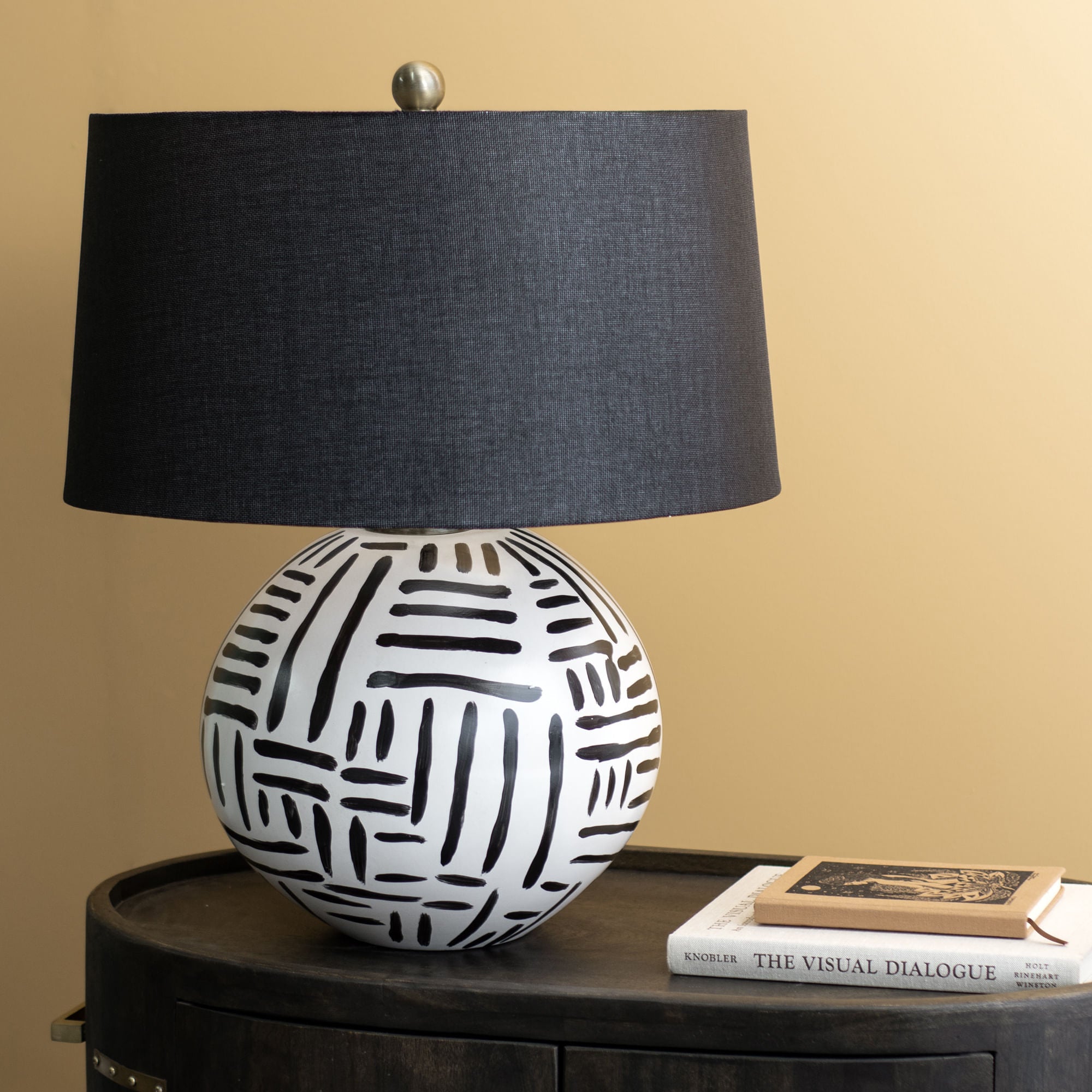 Milka table lamp with a round ceramic base featuring black and white geometric patterns and a black linen shade.