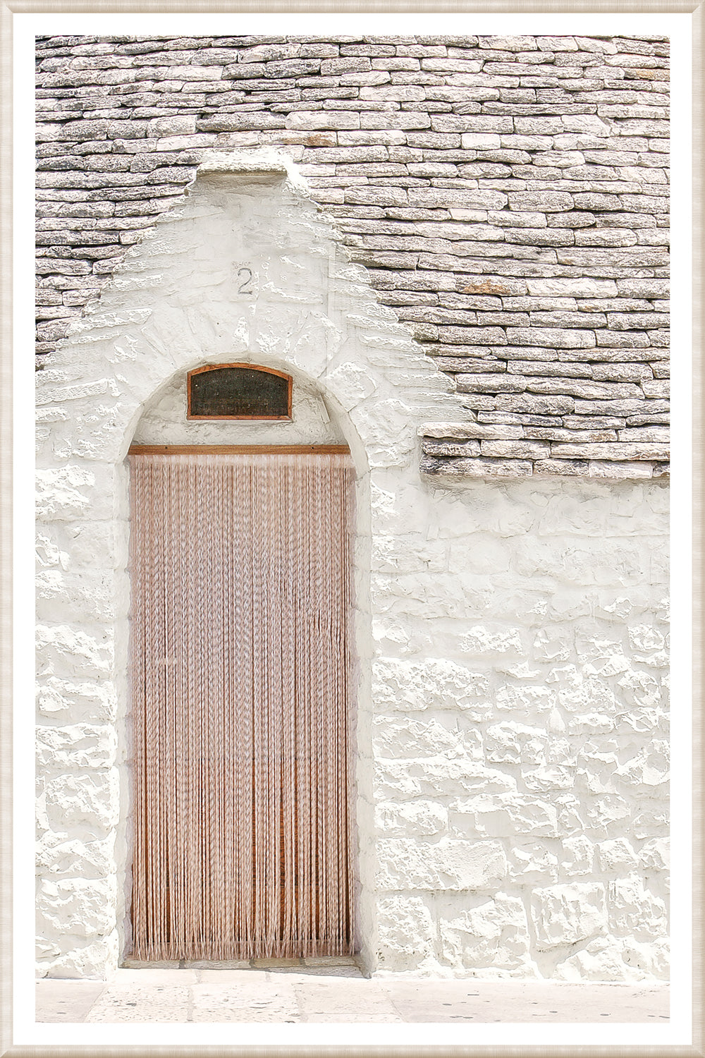 Masonry wall art featuring a white stone wall with a wooden door and hanging strands in Alberobello, Italy.