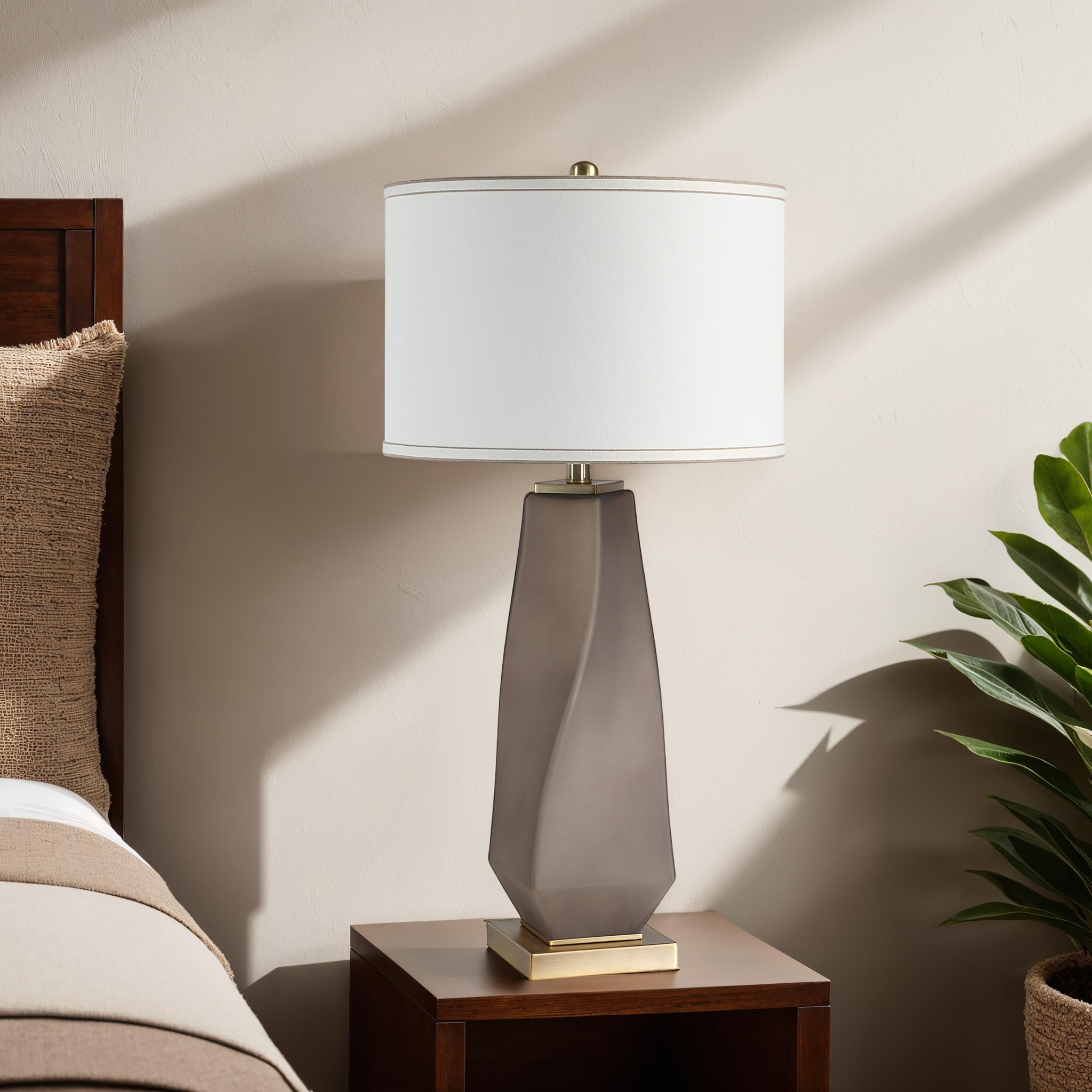 Mallorca table lamp on a nightstand beside a bed, with a plant in the background