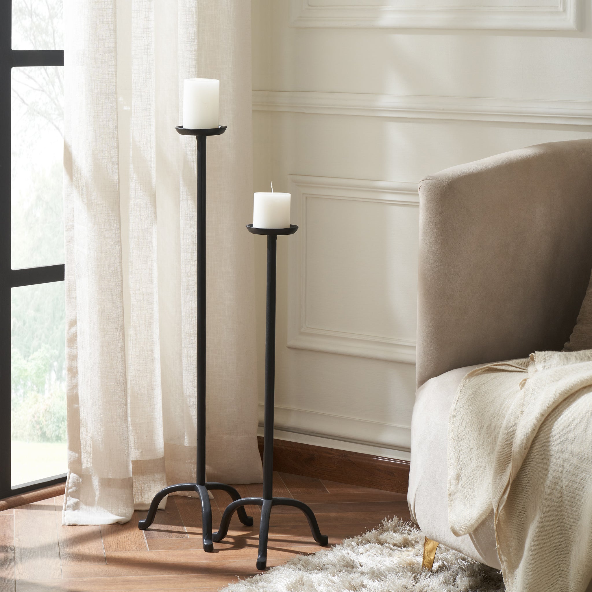 Agra candle holders in black metal displayed in a living room setting with white candles.