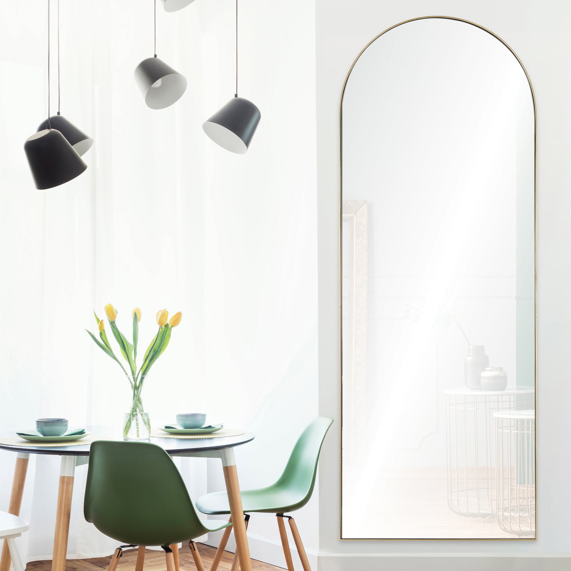 Thatcher Full Length Mirror in a bright room with a round table, green chairs, and hanging lights.