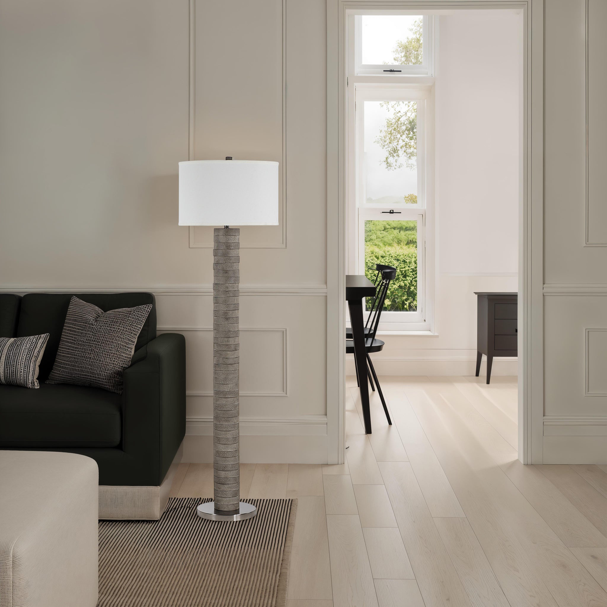 Moringa floor lamp next to a dark green sofa in a bright room with a view.