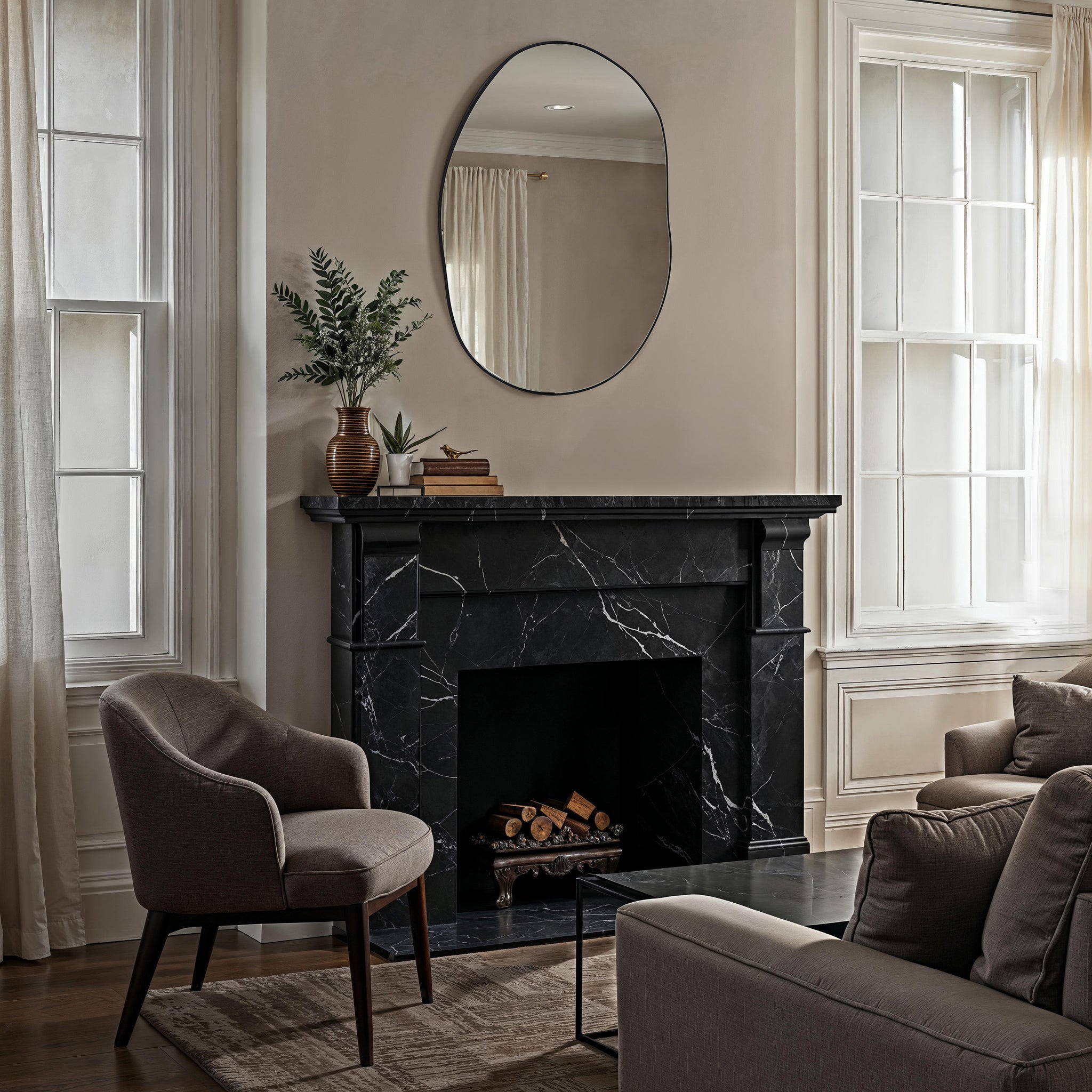 Messini mirror with an oval shape and black frame, hanging above a black marble fireplace in a cozy living room setting.