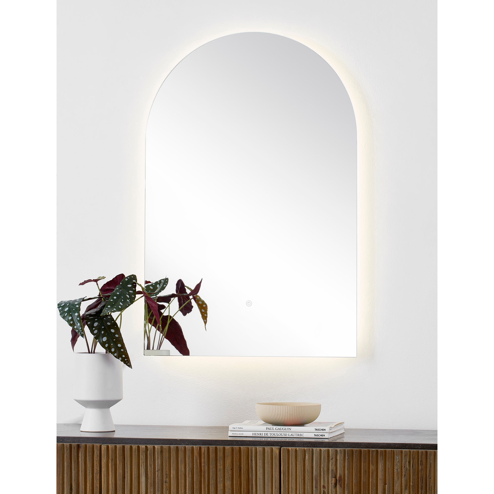 Blanca Led Mirror illuminated, displayed on a shelf with a plant and decor.