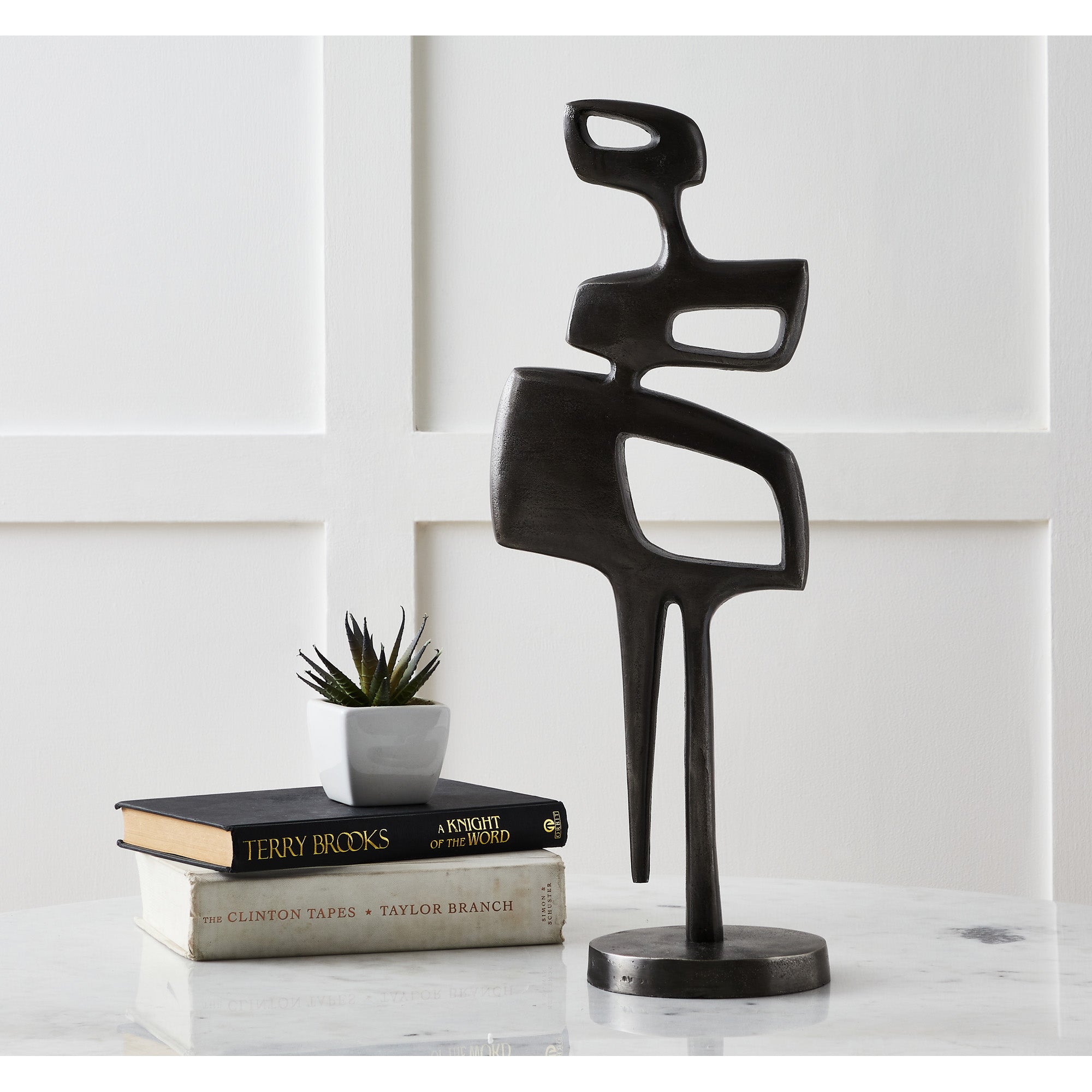 Pacino Indoor Aluminum Statue in Antique Nickel displayed on a table with books and a plant