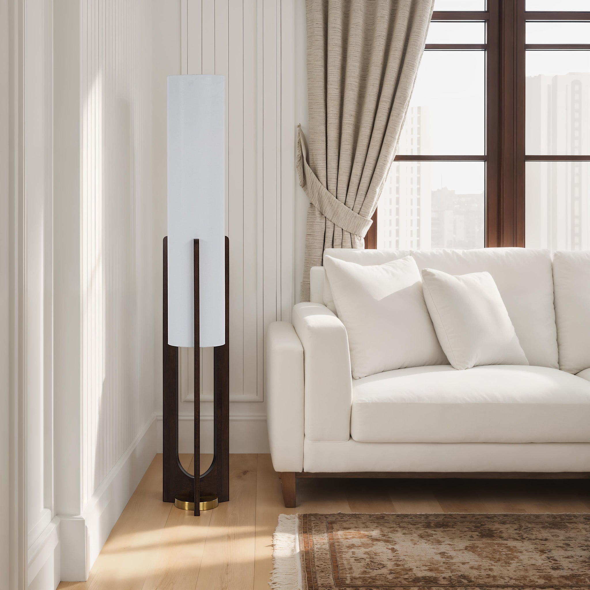 Mael floor lamp positioned beside a white sofa in a bright living room with large windows.
