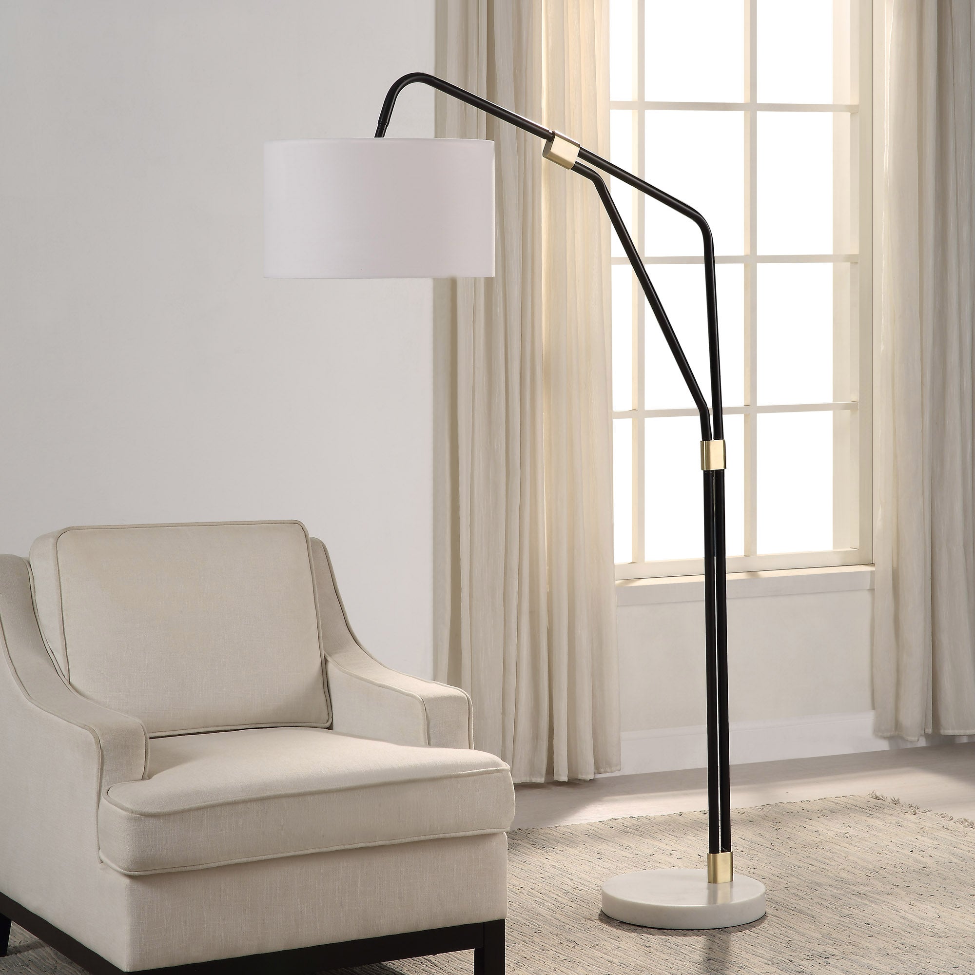 Wroxton Floor Lamp positioned next to a beige armchair, illuminating a bright room.