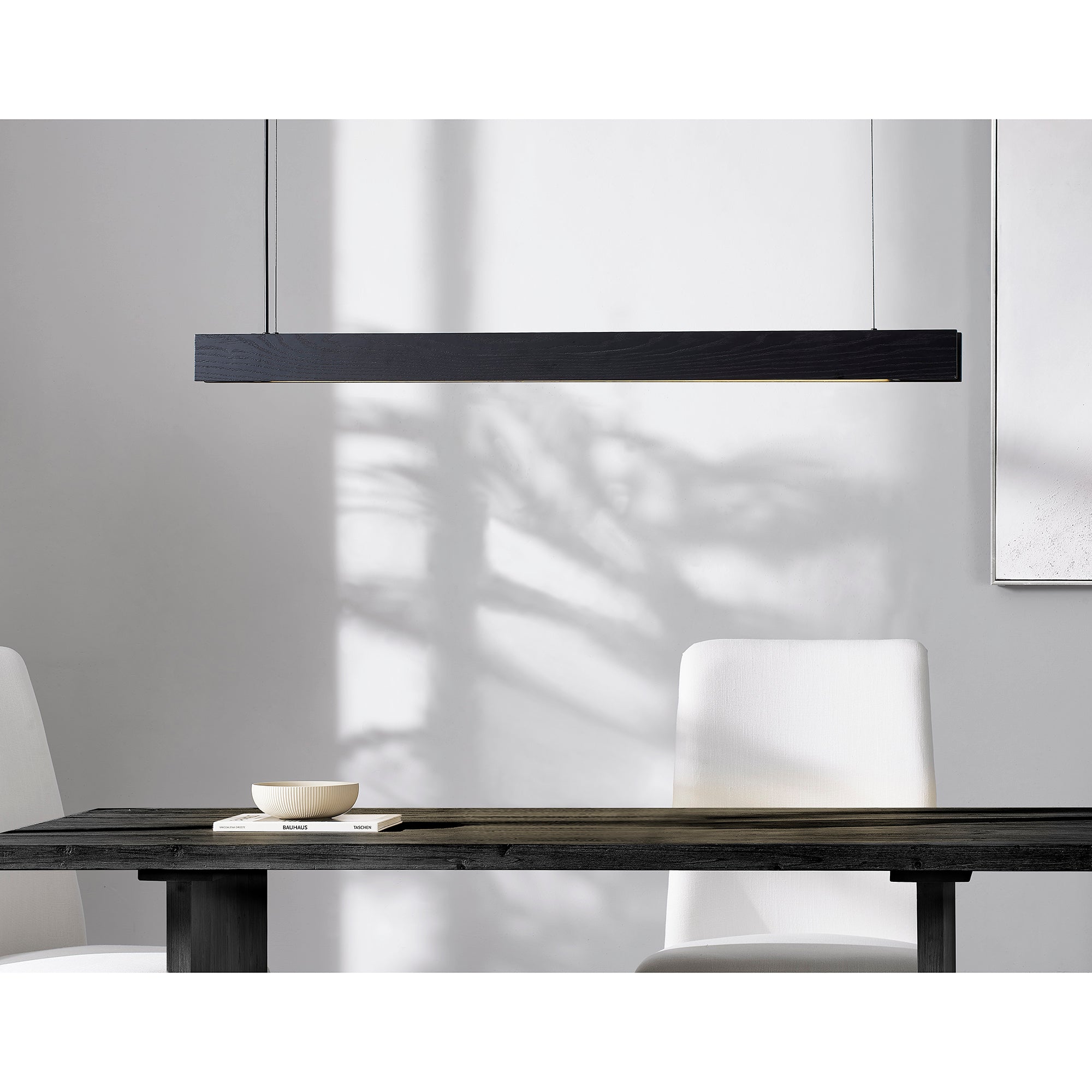 Taya Ceiling Fixture in black wood, linear design, hanging above a dark wooden table with white chairs.