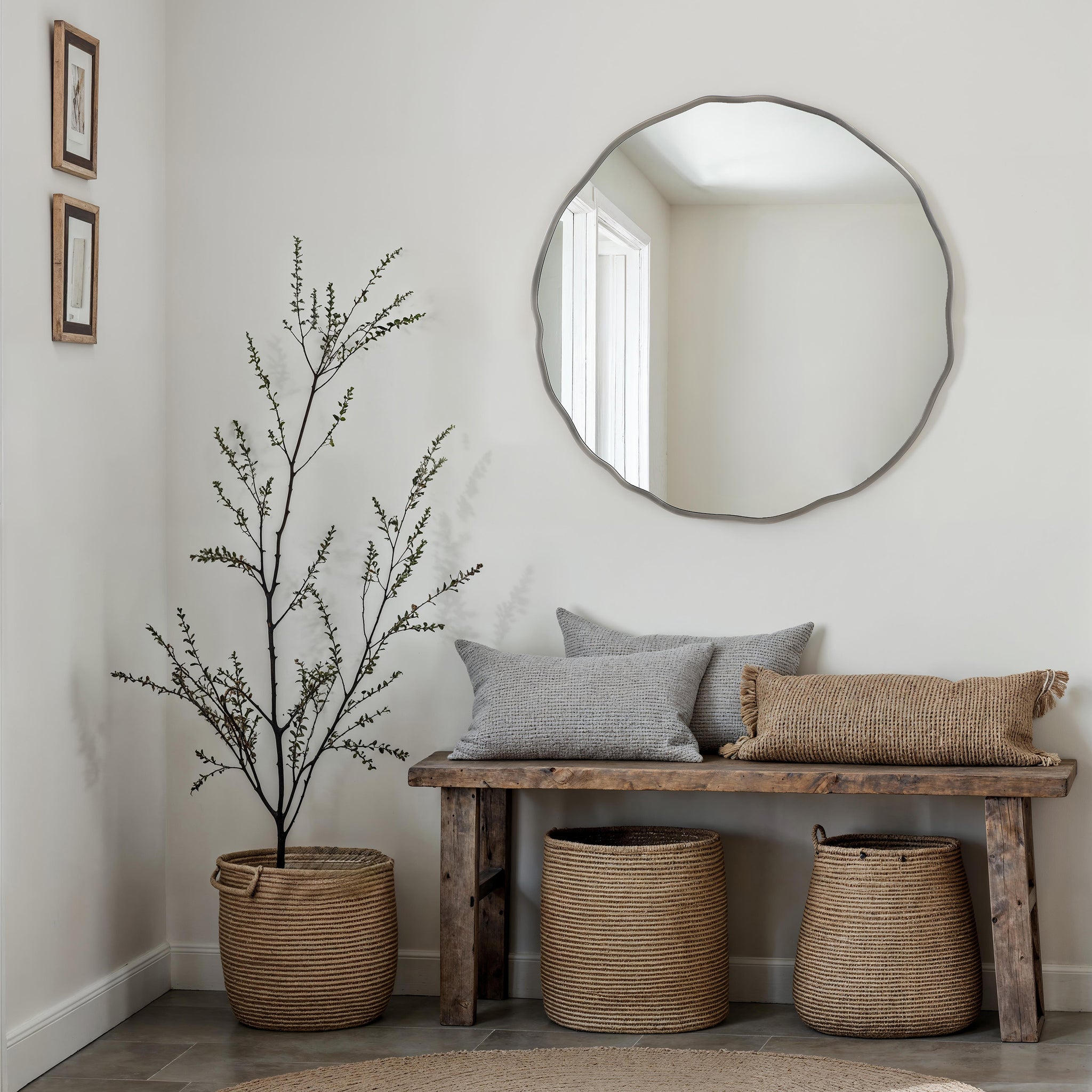 Cerro mirror with a wavy silver frame above a wooden bench, surrounded by decorative pillows and woven baskets.