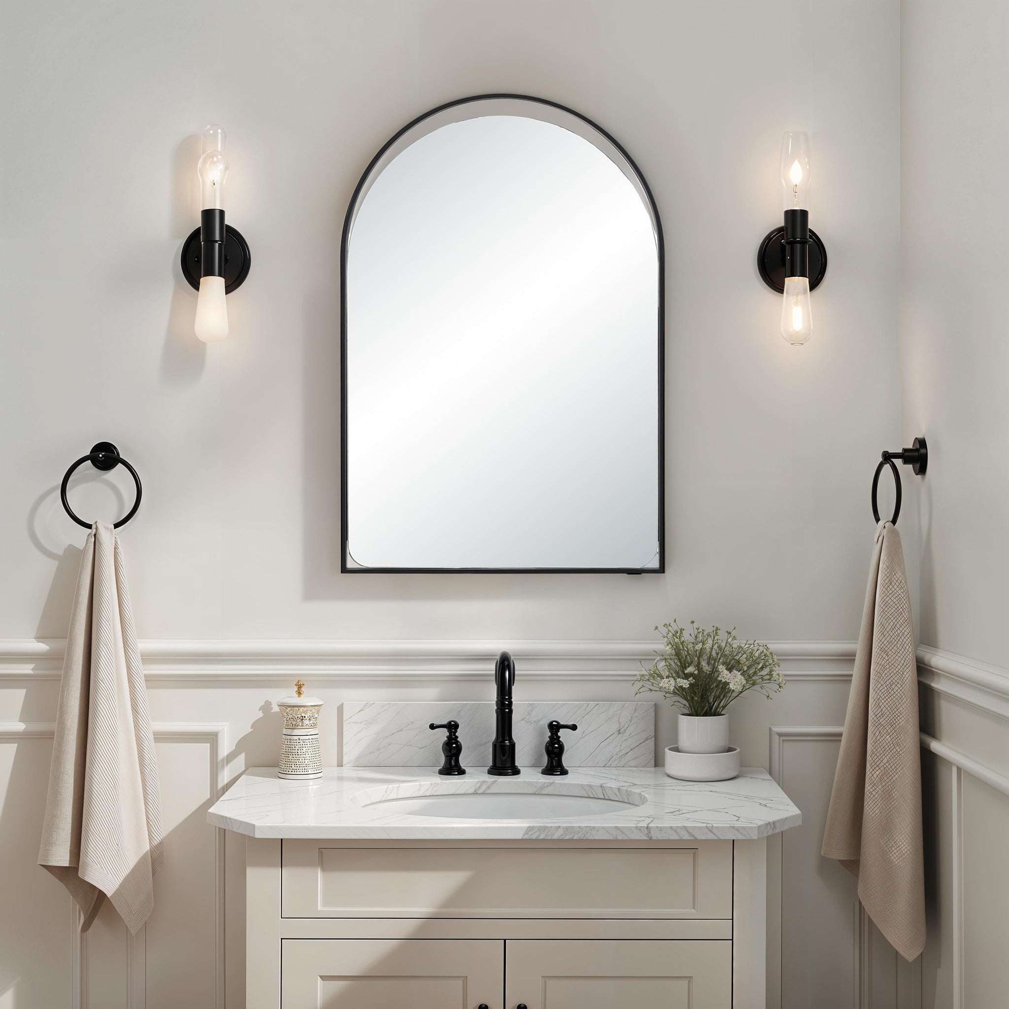 Maniola mirror mounted above a bathroom sink, complemented by stylish wall sconces.