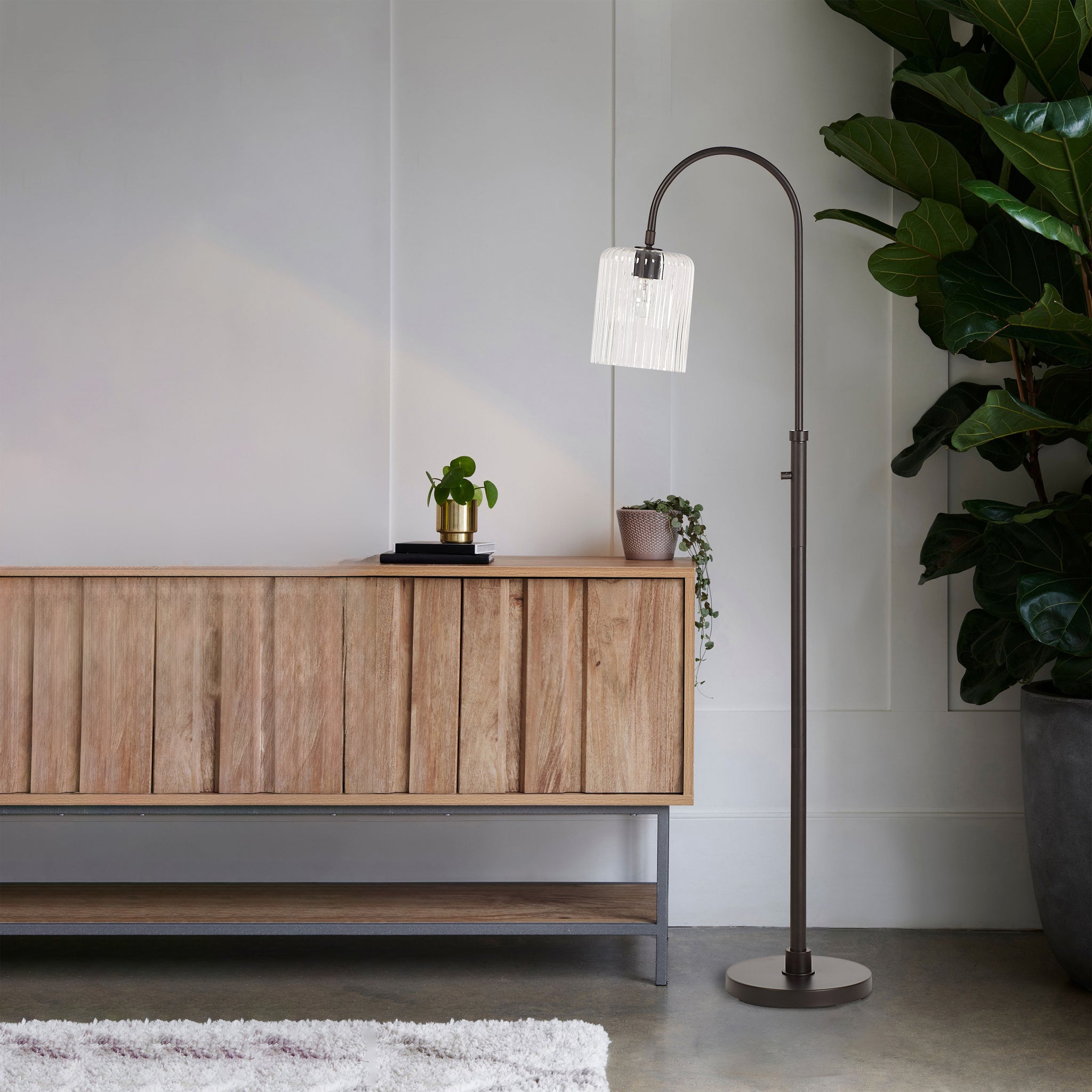 Danae floor lamp in a living room setting beside a wooden cabinet and plants.
