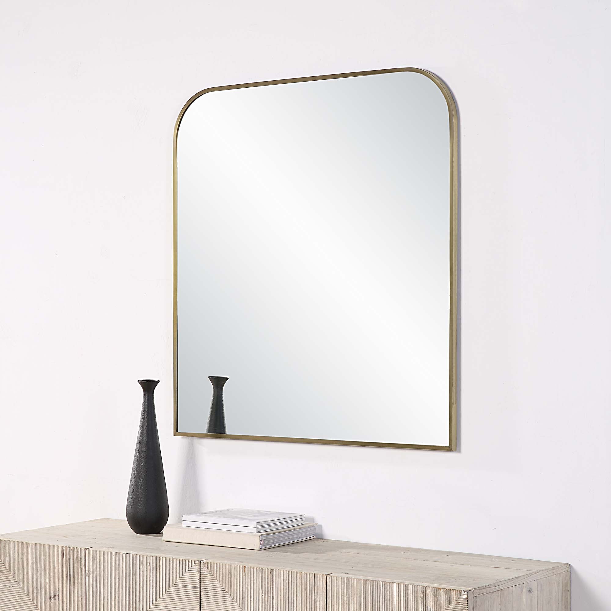 Joan Wall Mirror mounted on a wall above a wooden console with a black vase.