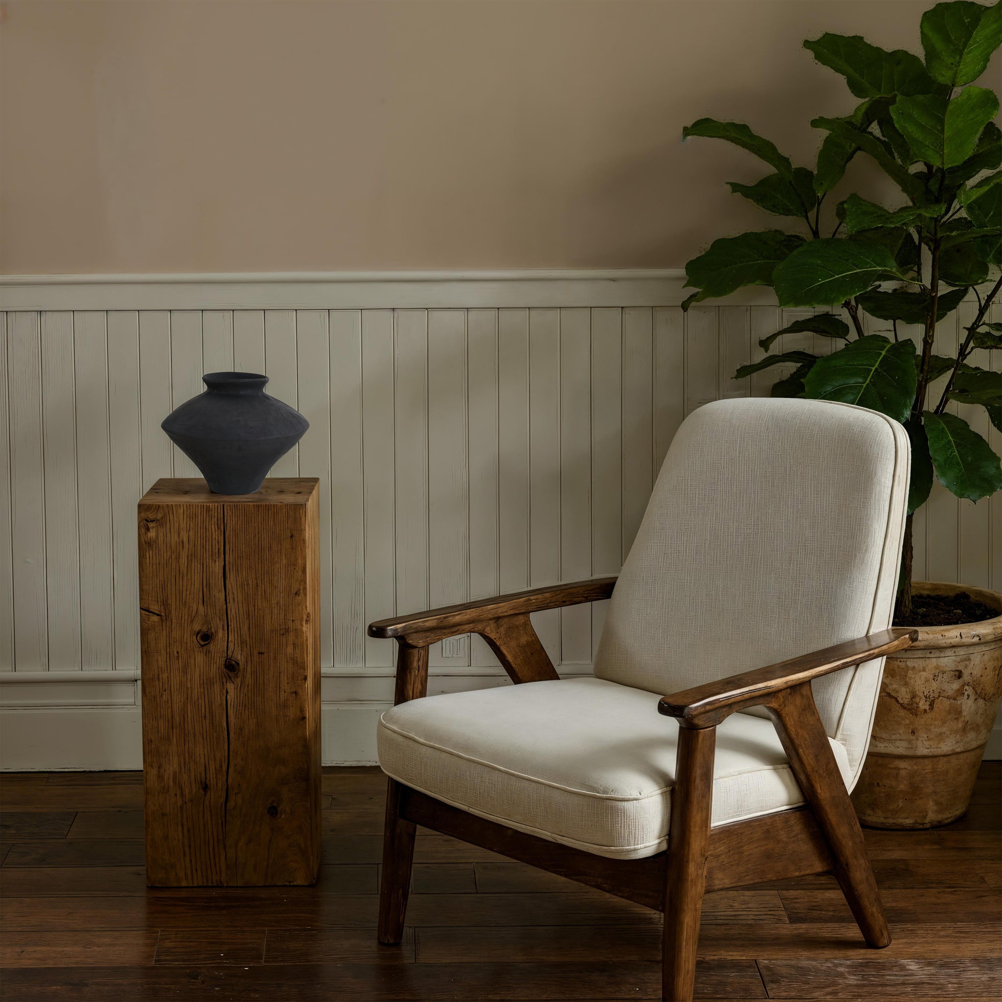 Mills vase by Renwil displayed on a wooden pedestal next to a chair and plant