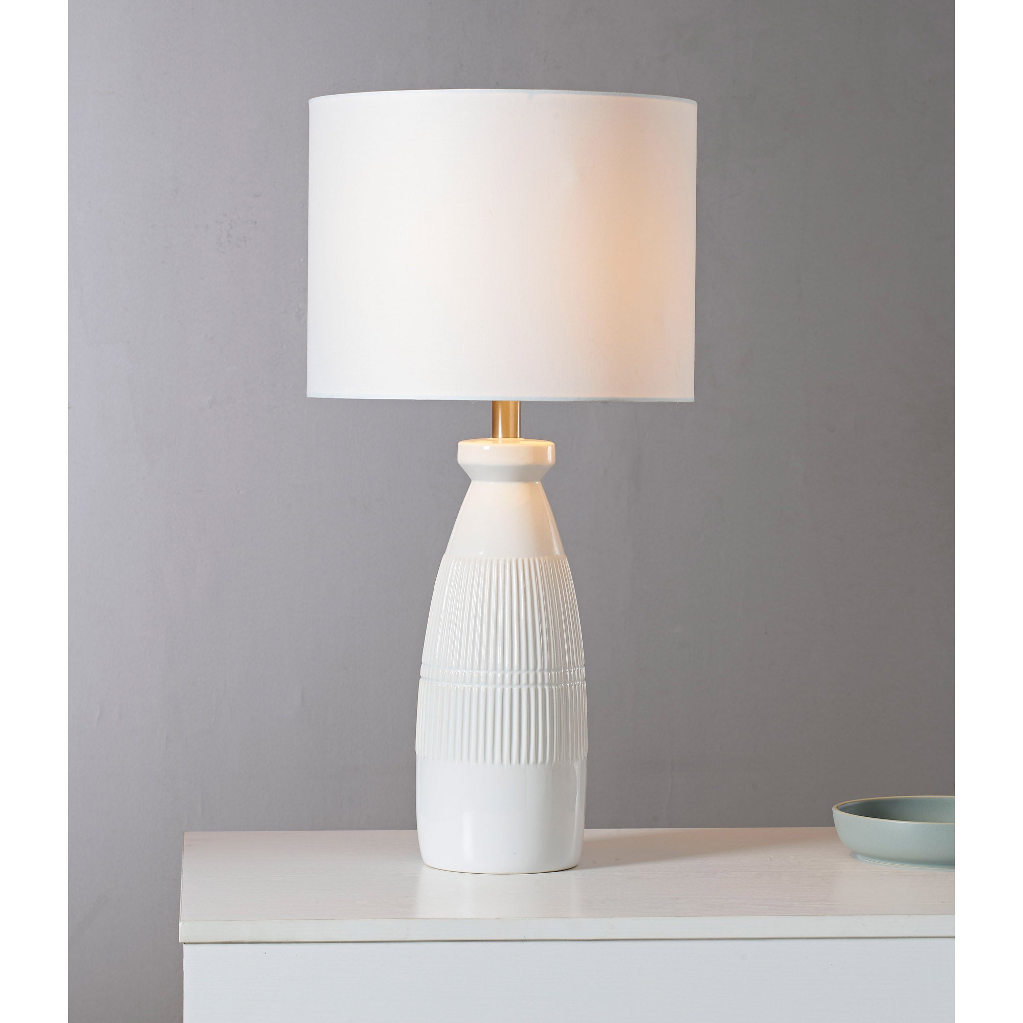 Nado Table Lamp glowing softly on a white surface, with a light gray backdrop and ribbed base