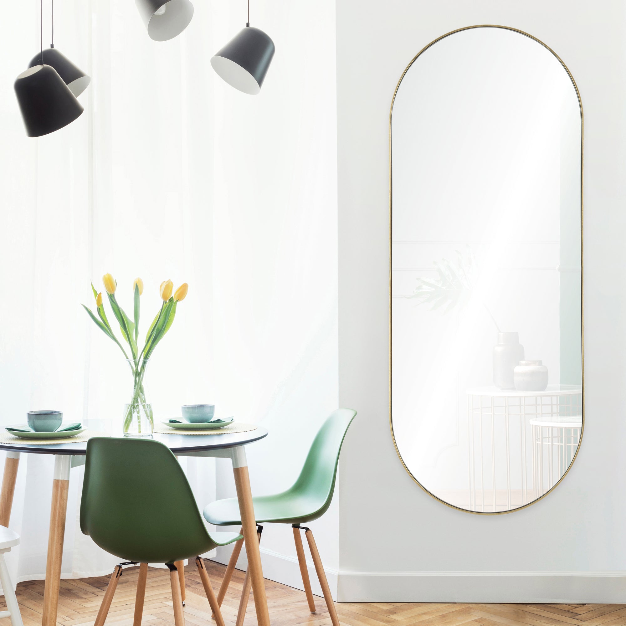 Marius Full Length Mirror in an oval shape with a gold frame, displayed in a bright dining area with green chairs.