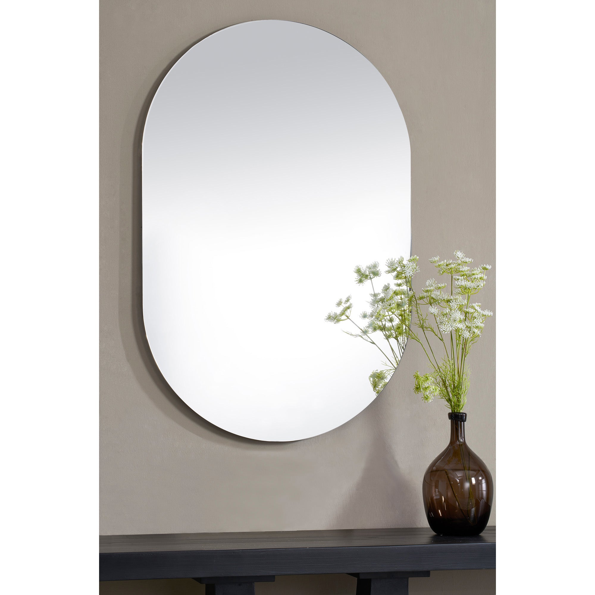 Salta mirror by Renwil, displayed on a wall with a vase of flowers in front, highlighting its oval shape.