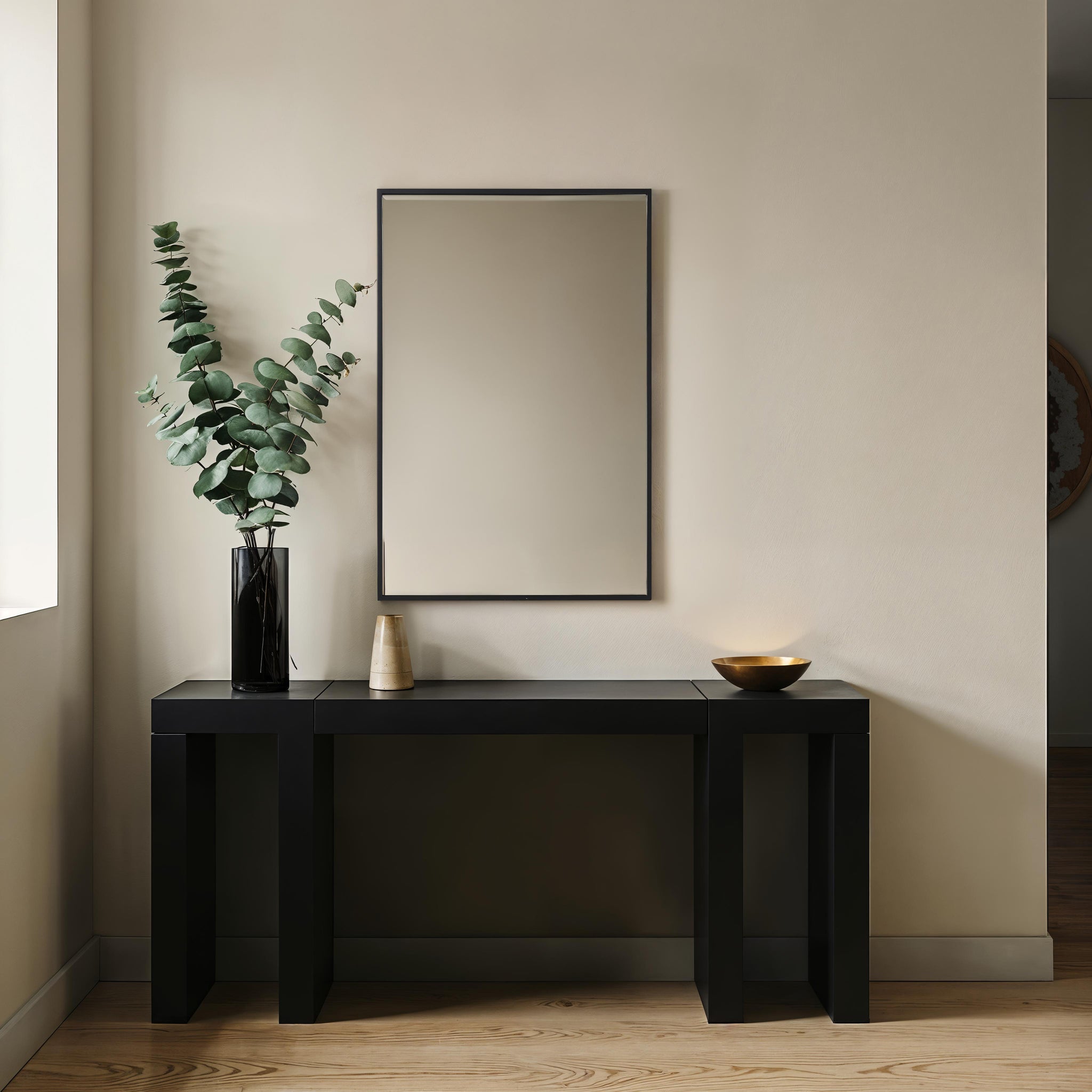 Agata mirror with a sleek black frame, displayed above a modern black console table with decorative items and greenery.