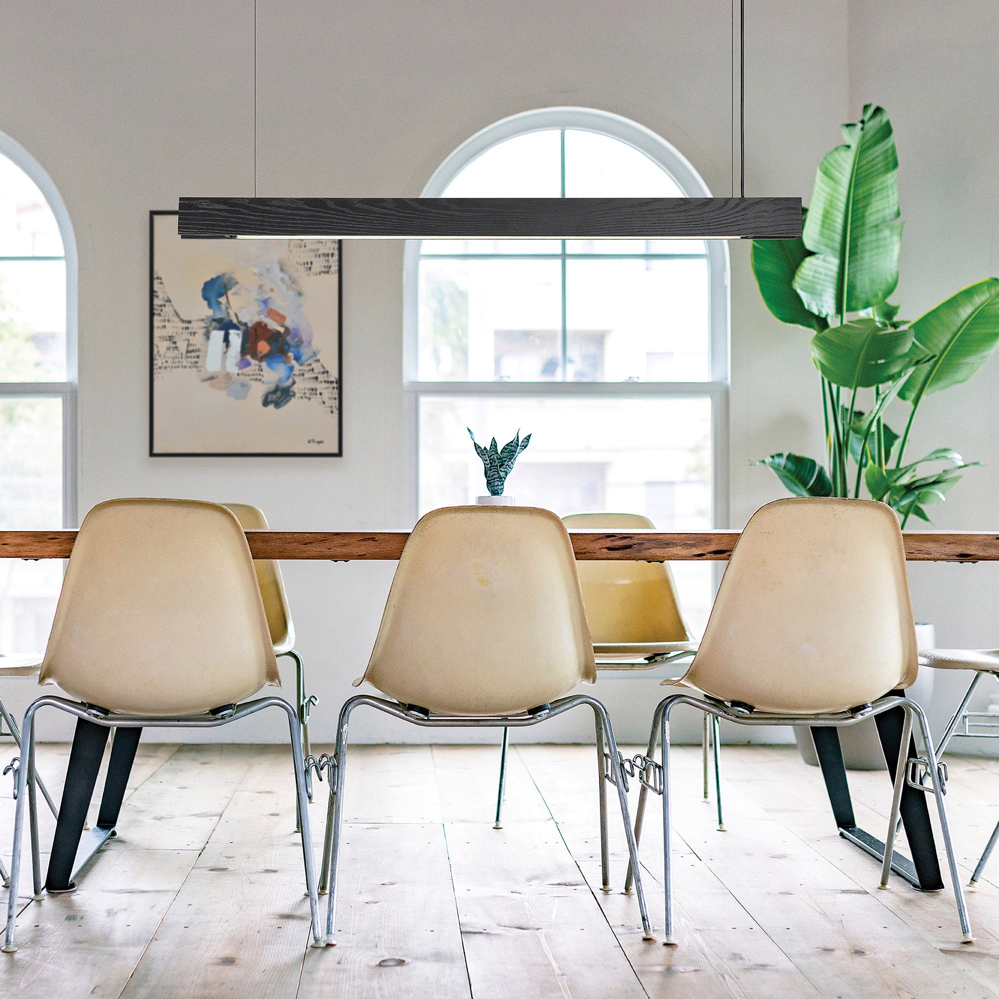 Taya Ceiling Fixture in black wood, linear style, suspended over a dining table with beige chairs and plants.