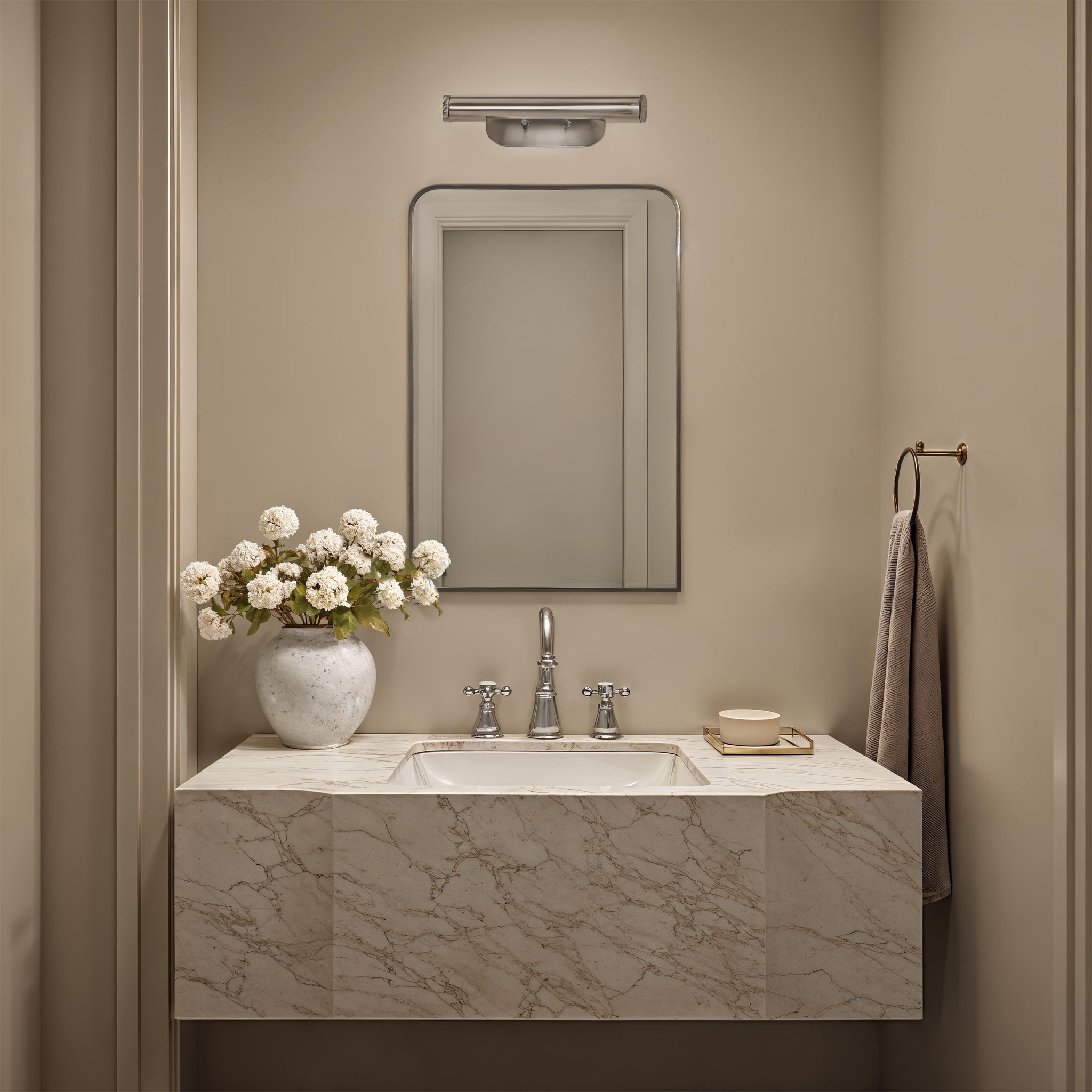 Jackline mirror above a marble sink in a bathroom, complemented by a vase of white flowers.