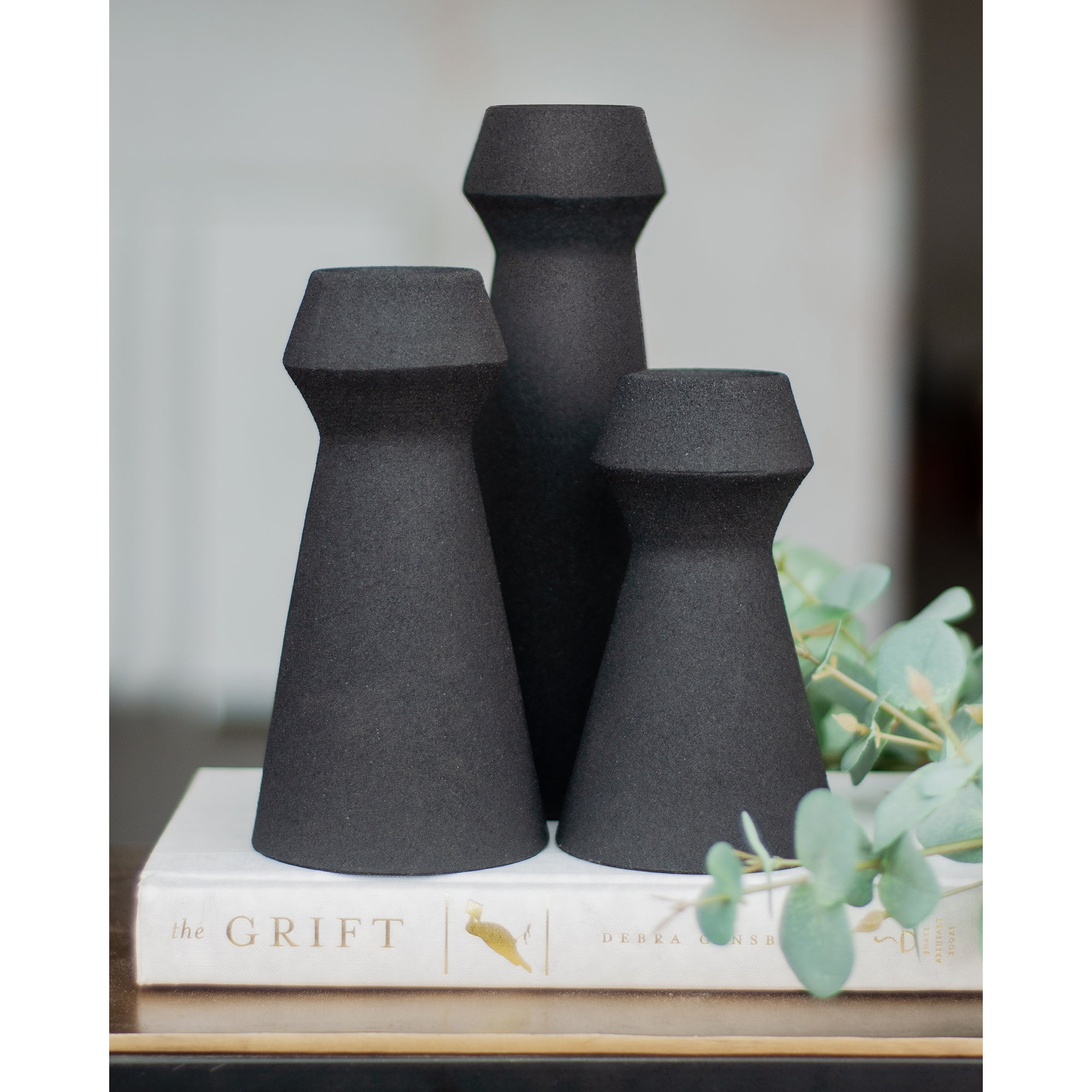 Granfeld Vase by Renwil in black, arranged on a book with greenery in the background.