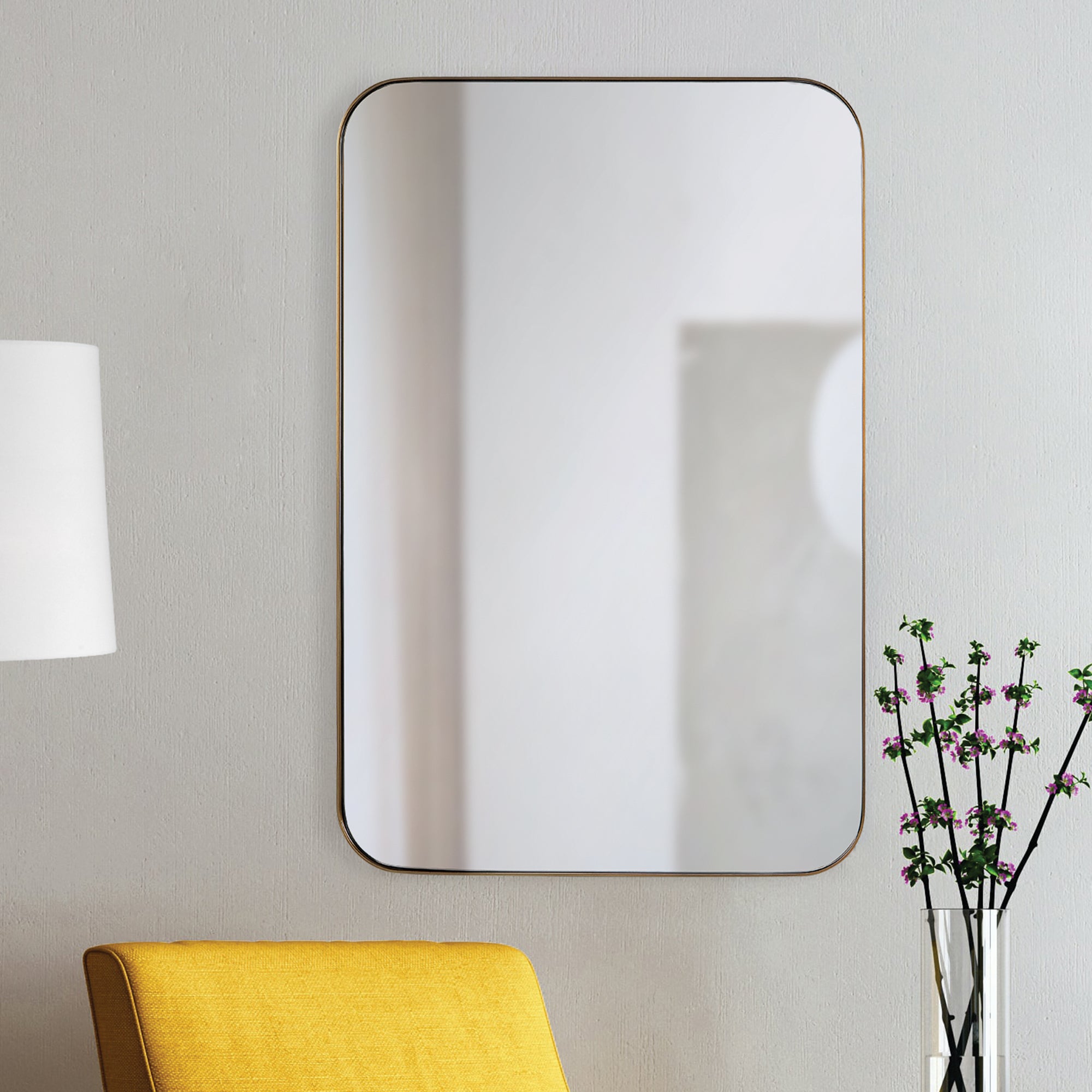 Edwin Wall Mirror mounted on a wall beside a yellow chair and a vase with flowers.