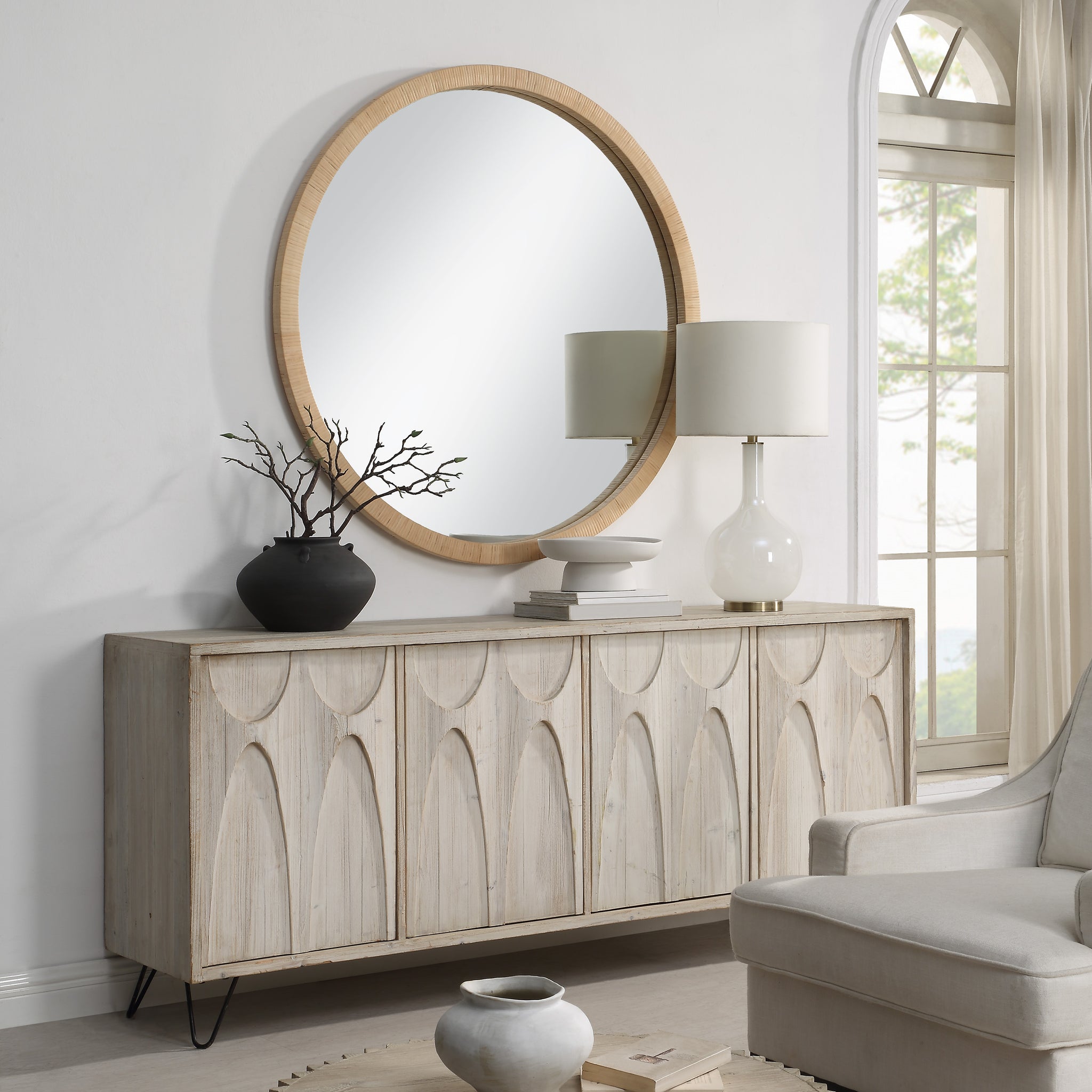 Rita mirror above a wooden sideboard, complemented by decor items and a lamp in a stylish interior.