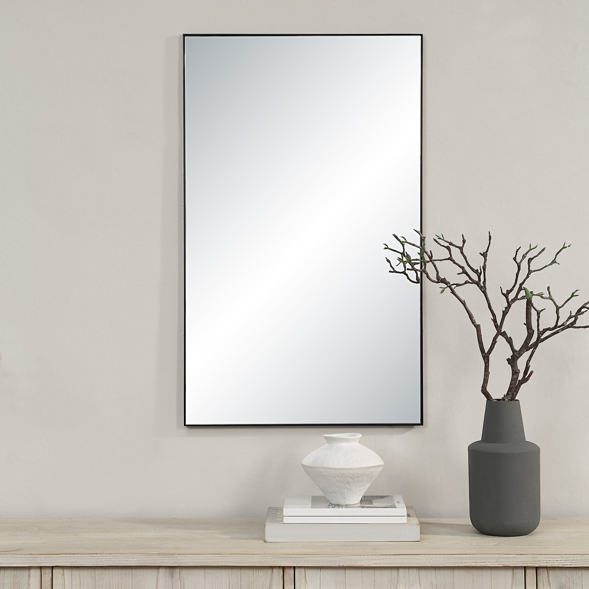 Loutro mirror by Renwil displayed on a wall, with decorative vase and branches on a wooden shelf.