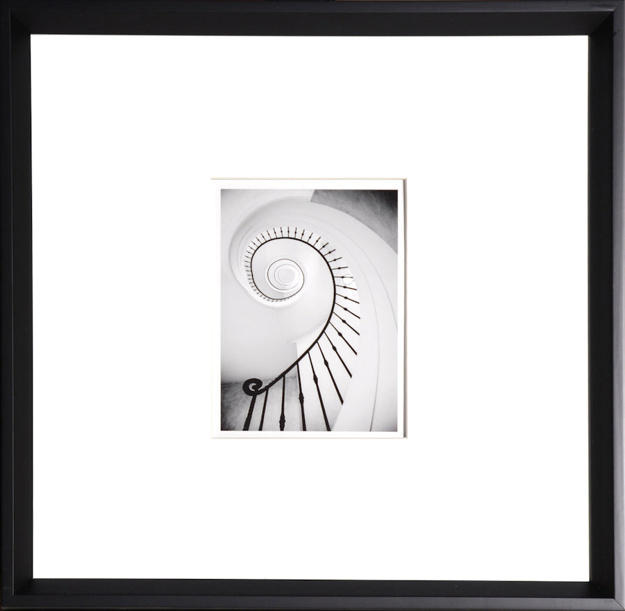 Spiral wall art featuring a black and white photo of a spiral staircase with a black frame.