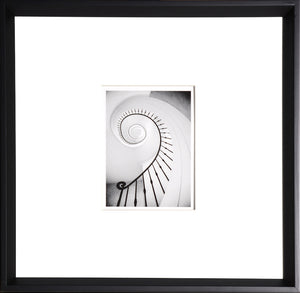 Spiral wall art featuring a black and white photo of a spiral staircase with a black frame.