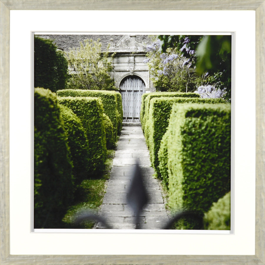 Jardin Vert Formel III wall art featuring a pathway lined with lush green hedges and a wooden door in the background.