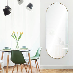 Marius mirror with a gold frame, displayed on a white wall next to a dining table with green chairs and yellow tulips.