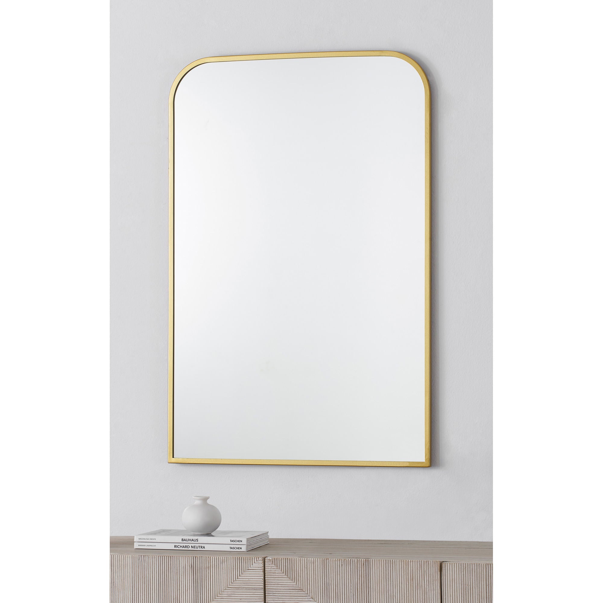 Merrimack mirror with a sleek gold frame, featuring a rounded top and a clear reflective surface, displayed against a light wall.