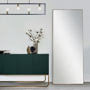 Northern mirror with a sleek gold frame, positioned beside a dark green cabinet and decorative vase.