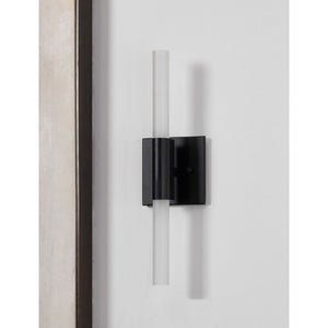 Lina wall sconce by Renwil, mounted on a wall, featuring matte black base and frosted glass tube.