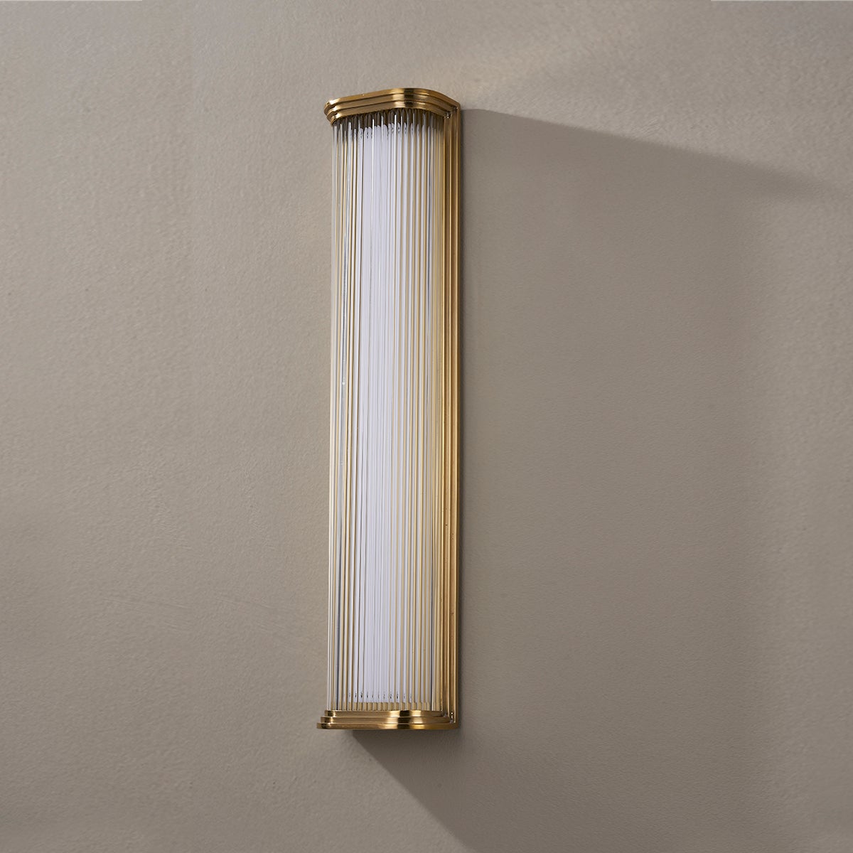 Newburgh Bath And Vanity 5.25" x 24.5" in aged brass shown from the front to reveal the arm spread and shade silhouette.
