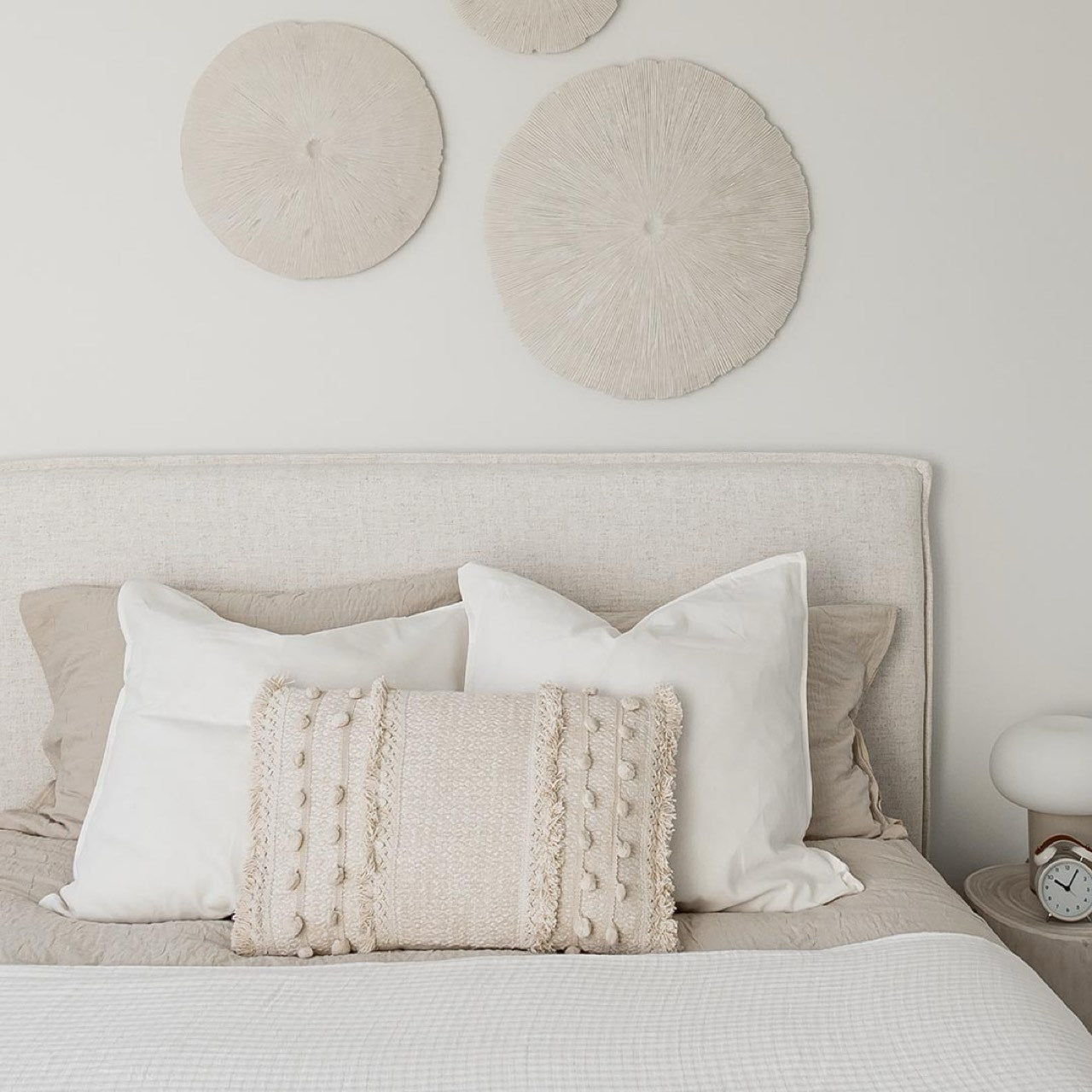 Neatly made bed with decorative pillows and circular wall art in a bedroom setting.