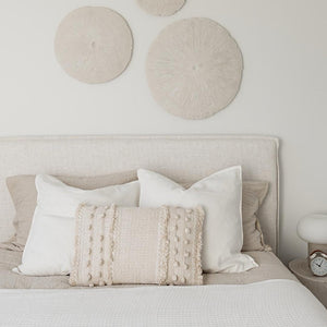Neatly made bed with decorative pillows and circular wall art in a bedroom setting.