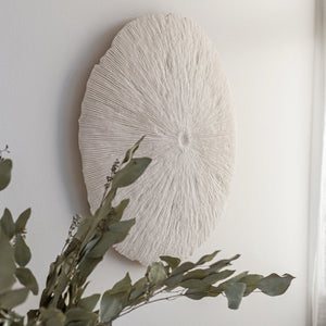 Decorative wall art with a sunburst pattern on a plain wall, featuring green foliage.