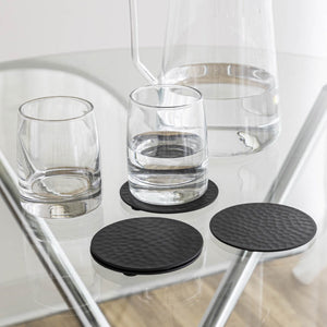 Black coasters on a glass table with glasses of water