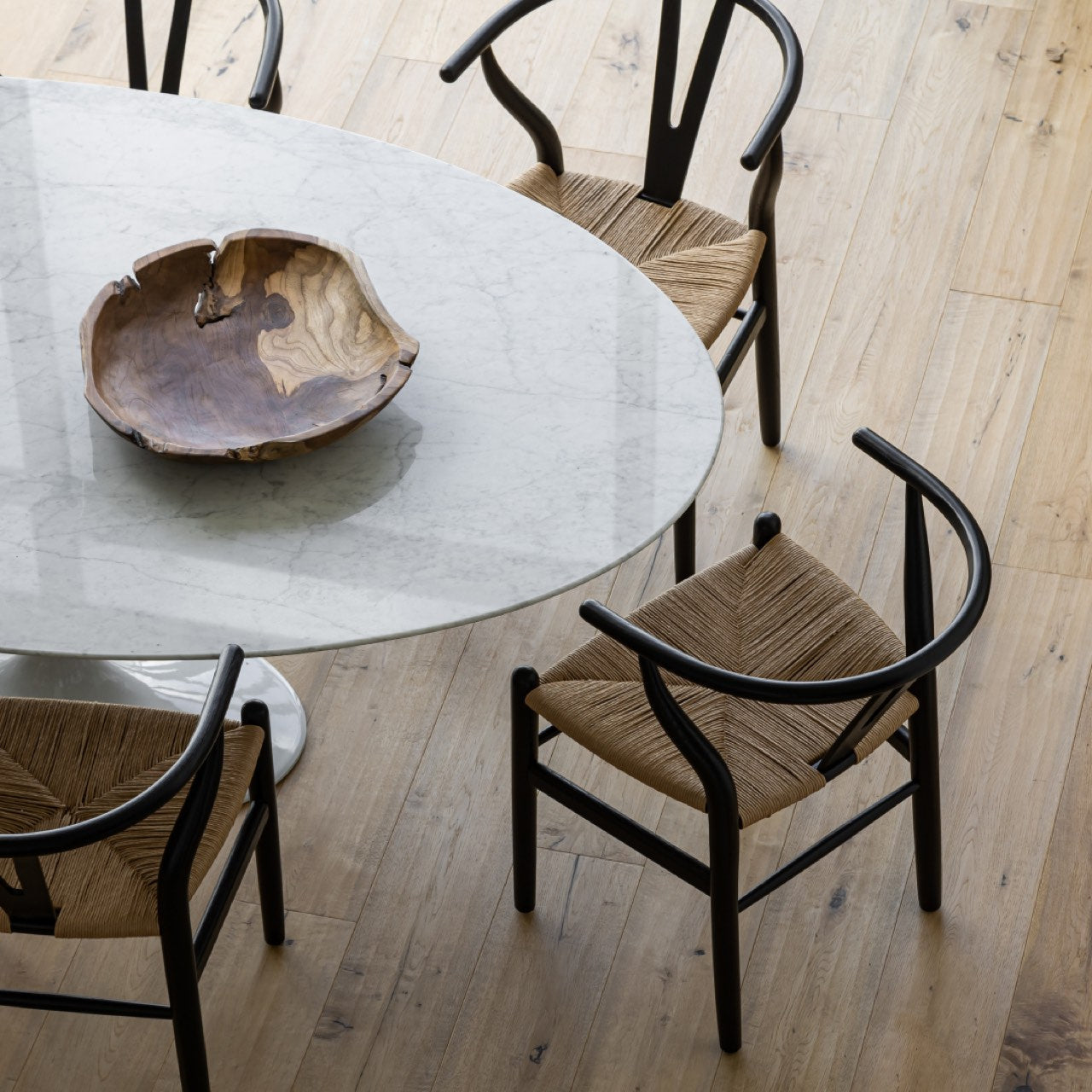 Round glass dining table with a wooden bowl and four chairs on a wooden floor.