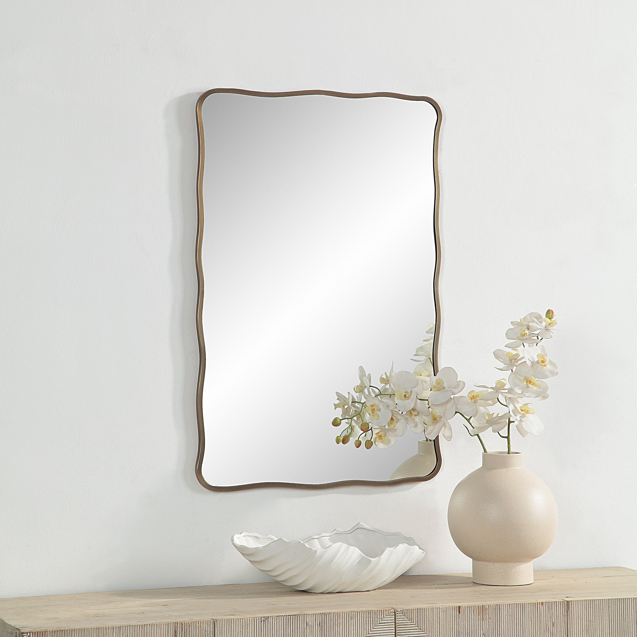 Basel Wall Mirror displayed on a wall with a vase of flowers and decorative bowl.
