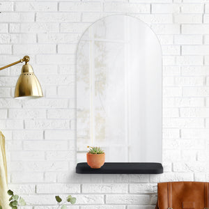 Lucila Wall Mirror mounted on a white brick wall with a small plant on the shelf