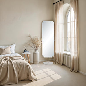 Mandra mirror in a cozy bedroom setting, positioned beside a bed with neutral decor and natural light.